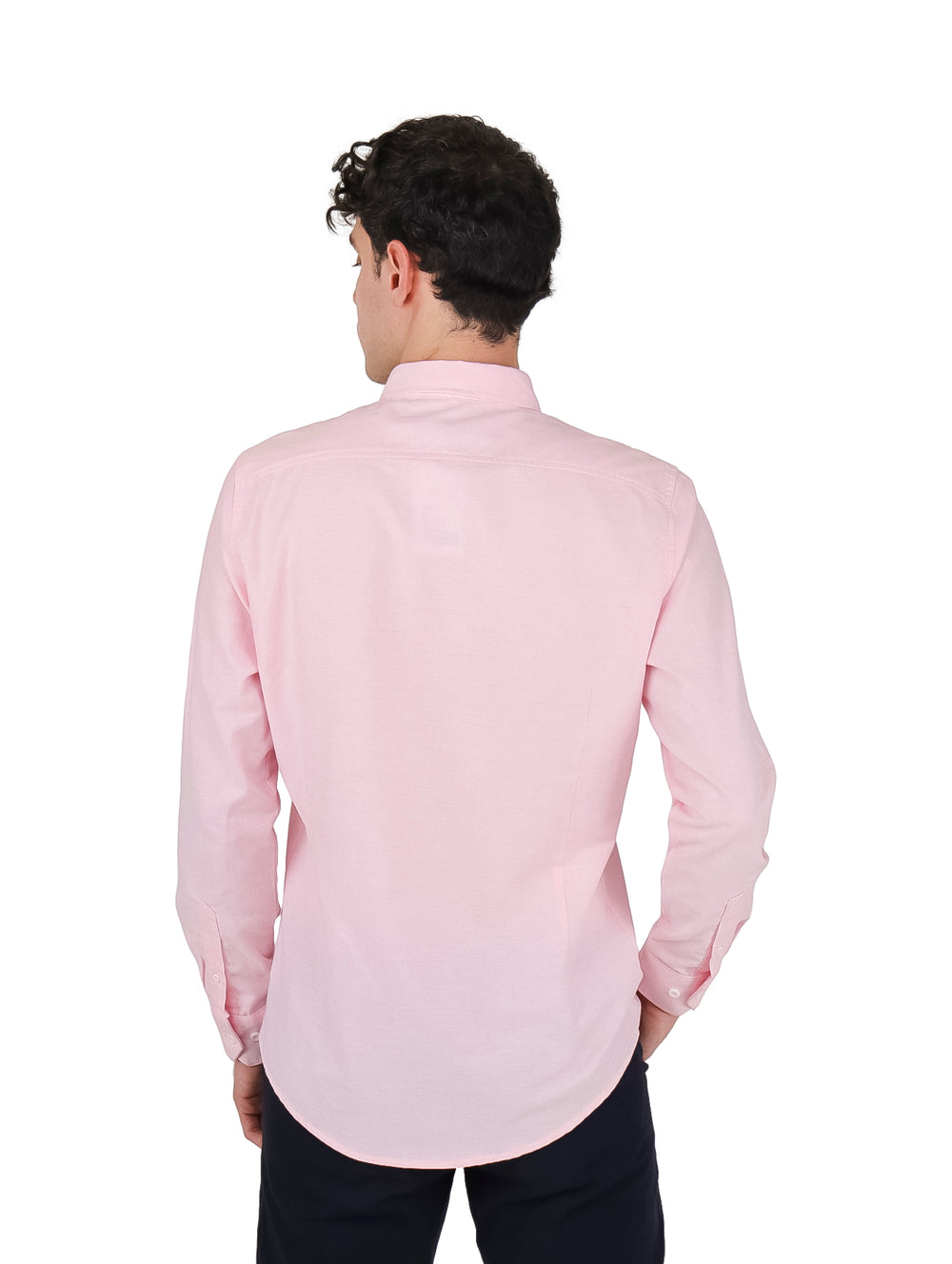 Hombre vistiendo una camisa Oxford de color rosa claro con manga larga y pantalones oscuros.