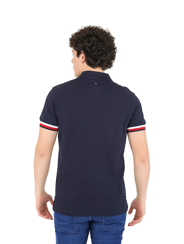 Hombre vistiendo polo Tommy Hilfiger color azul marino con detalles rojos y blancos en las mangas y logotipo en el pecho.