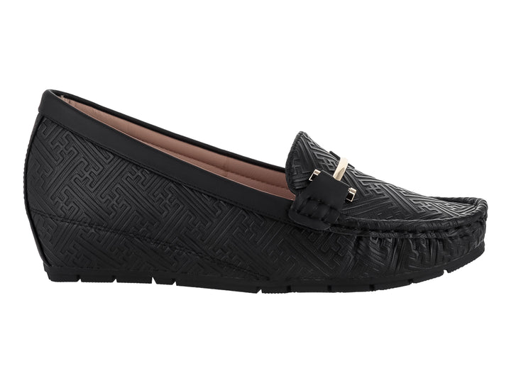 Zapato tipo mocasín color negro con textura grabada y detalle metálico dorado en la parte superior.