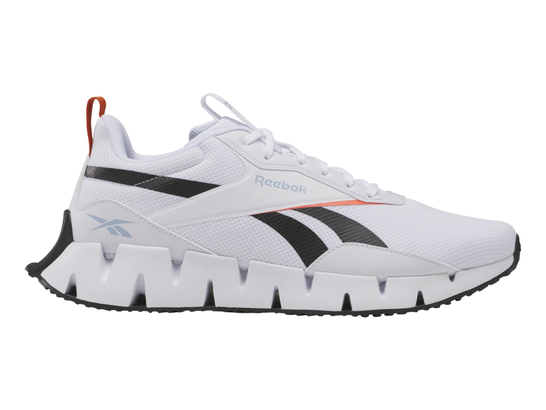 Tenis deportivos Reebok blancos con detalles negros y rojos y suela blanca con diseño zigzag.