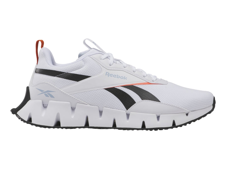 Tenis deportivos Reebok blancos con detalles negros y rojos y suela blanca con diseño zigzag.