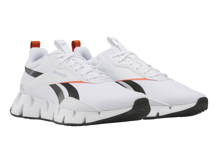 Tenis deportivos Reebok blancos con detalles negros y rojos y suela blanca con diseño zigzag.