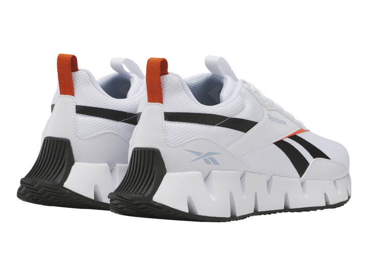 Tenis deportivos Reebok blancos con detalles negros y rojos y suela blanca con diseño zigzag.