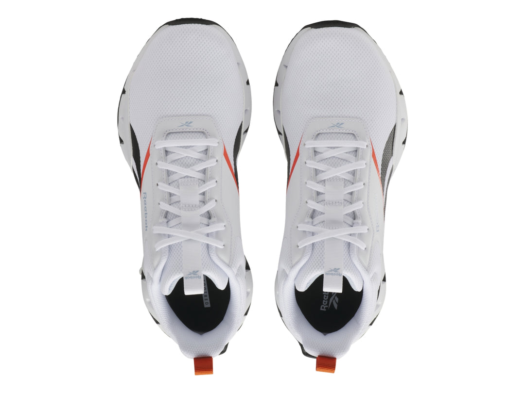 Tenis deportivos Reebok blancos con detalles negros y rojos y suela blanca con diseño zigzag.