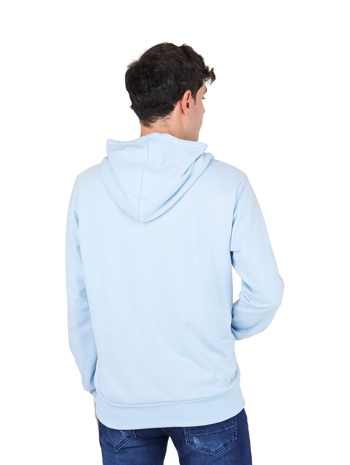 Hombre vistiendo una sudadera con capucha color azul cielo con estampado frontal y pantalones vaqueros azules.
