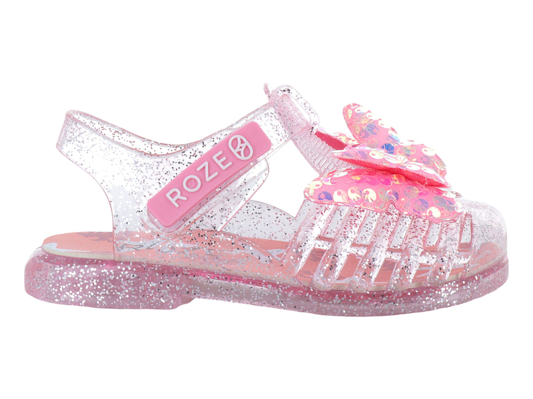 Sandalias infantiles color rosa con glitter, material transparente y un moño decorativo en la parte superior.