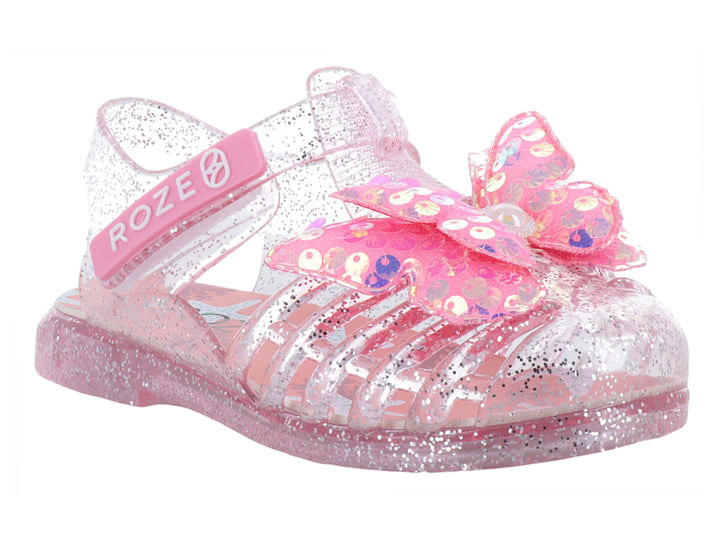 Sandalias infantiles color rosa con glitter, material transparente y un moño decorativo en la parte superior.