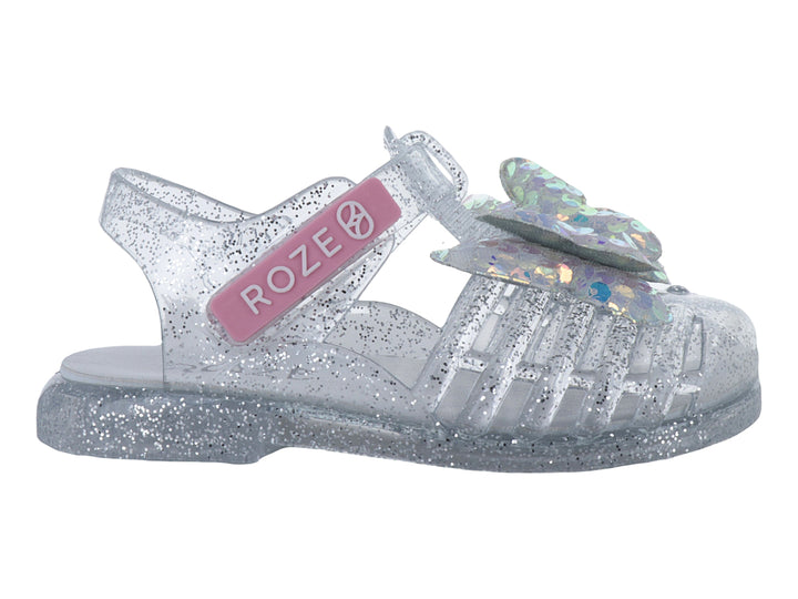 Sandalia infantil color plata con glitter y un moño iridiscente en la parte frontal.
