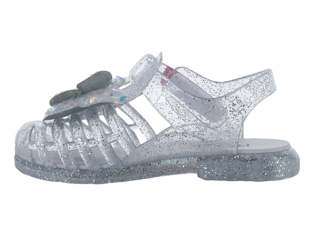Sandalia infantil color plata con glitter y un moño iridiscente en la parte frontal.