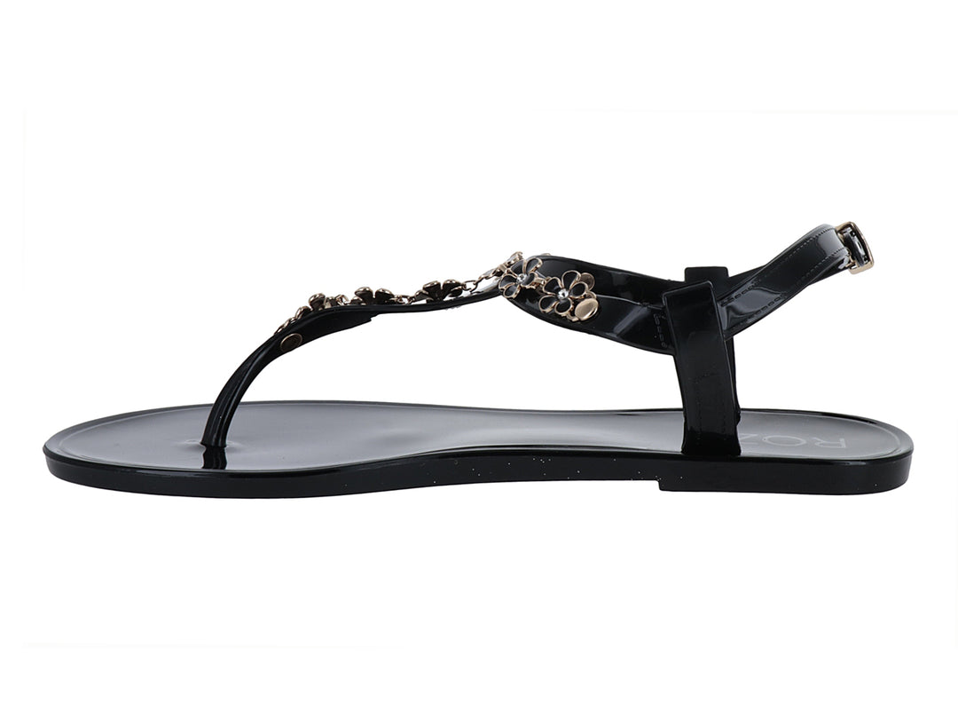Sandalia negra de suela plana con detalles decorativos de flores doradas y correa ajustable al tobillo.