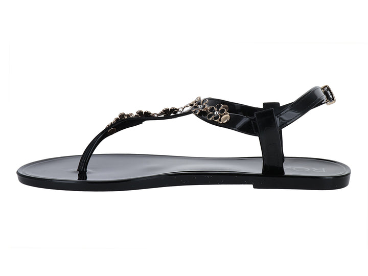 Sandalia negra de suela plana con detalles decorativos de flores doradas y correa ajustable al tobillo.