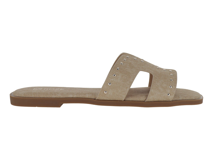 Sandalias planas color beige para mujer con detalles de remaches metálicos en la banda superior.