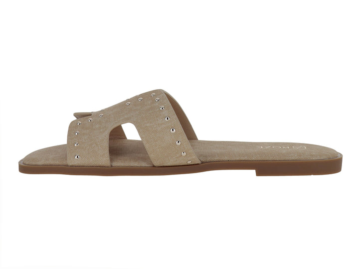 Sandalias planas color beige para mujer con detalles de remaches metálicos en la banda superior.