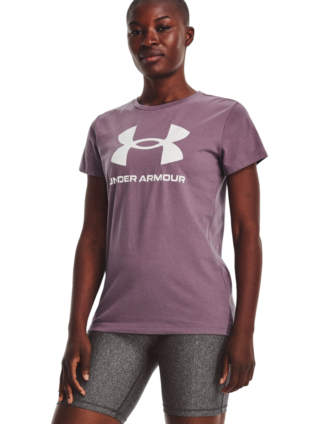 Mujer vistiendo camiseta deportiva morada de manga corta con logo blanco de Under Armour y shorts grises.