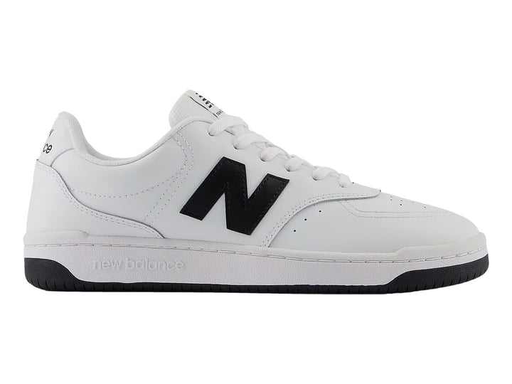 Tenis New Balance blancos con logotipo N en negro y suela negra, vista lateral.