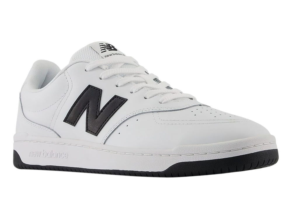 Tenis New Balance blancos con logotipo N en negro y suela negra, vista lateral.