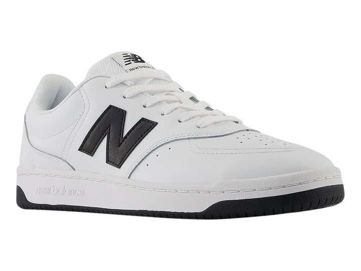 Tenis New Balance blancos con logotipo N en negro y suela negra, vista lateral.