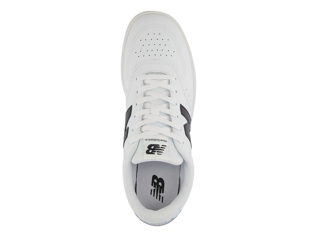 Tenis New Balance blancos con logotipo N en negro y suela negra, vista lateral.
