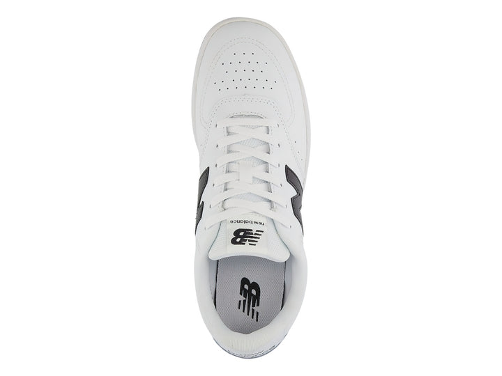 Tenis New Balance blancos con logotipo N en negro y suela negra, vista lateral.