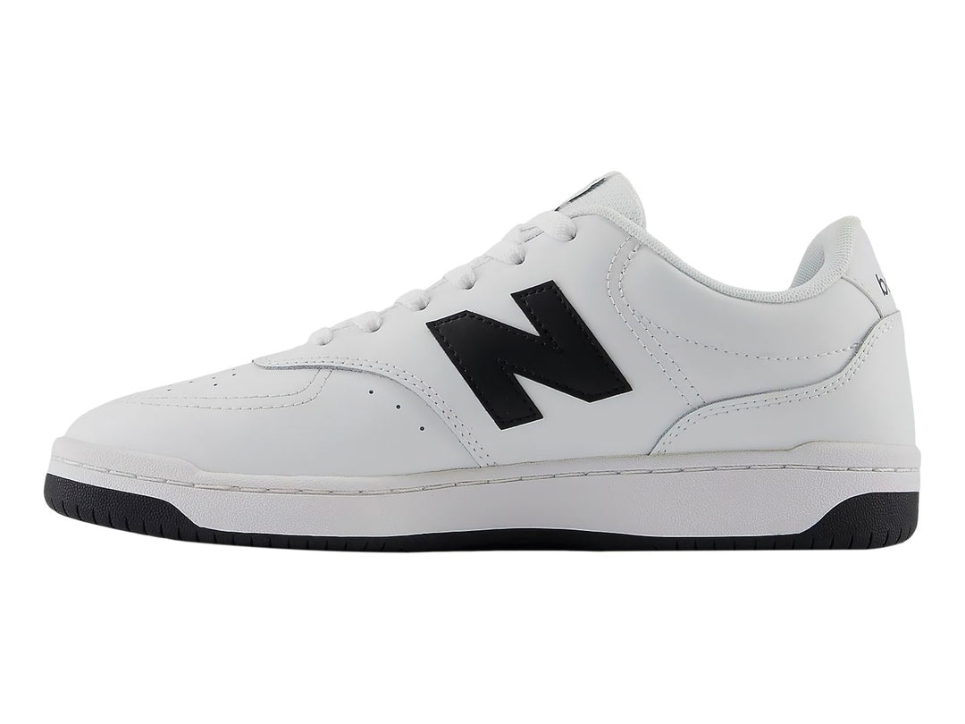Tenis New Balance blancos con logotipo N en negro y suela negra, vista lateral.