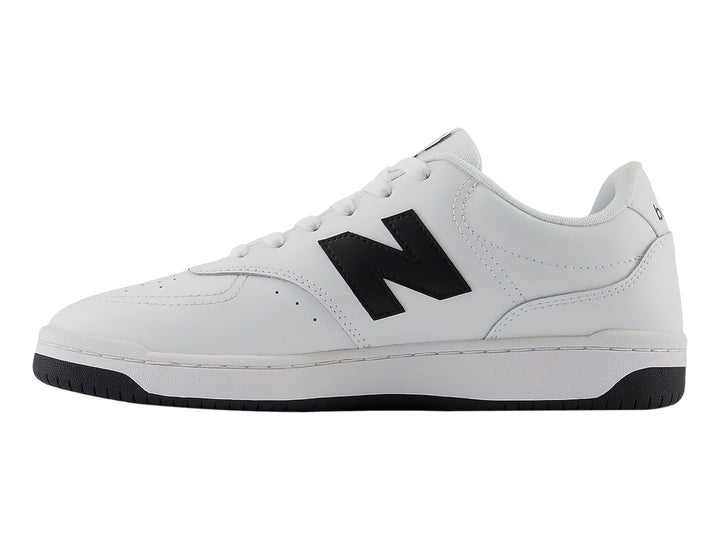 Tenis New Balance blancos con logotipo N en negro y suela negra, vista lateral.