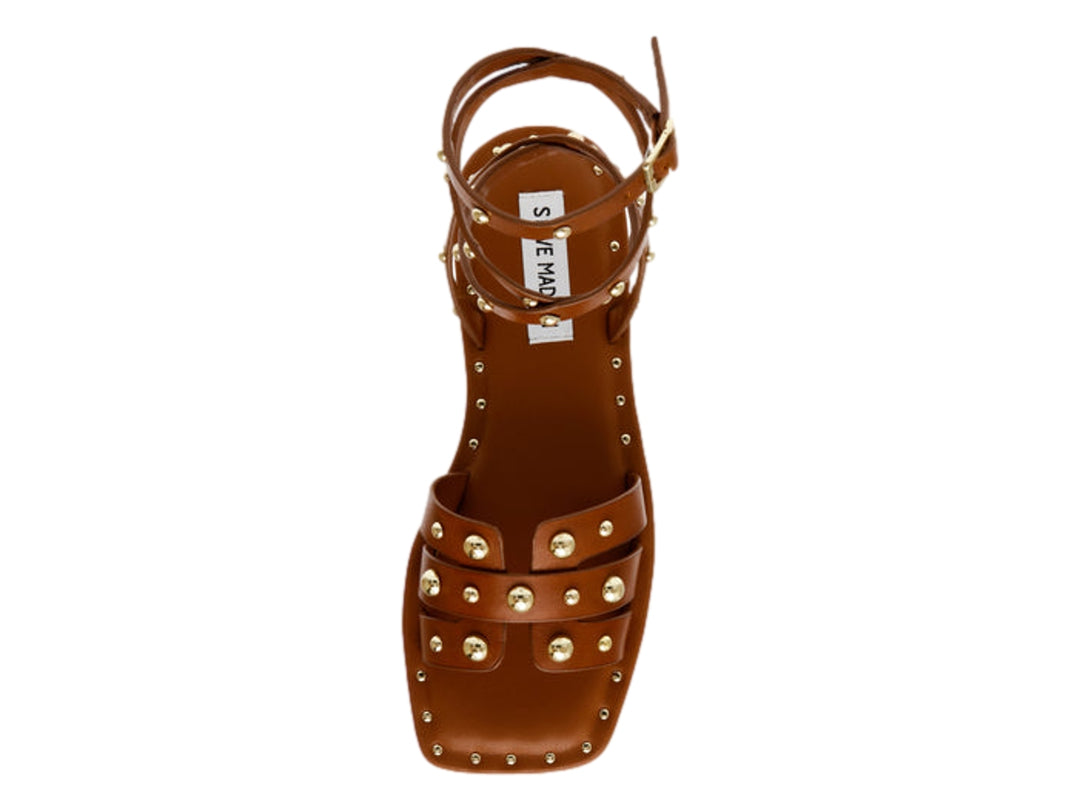 Sandalia plana color cognac de Steve Madden con tiras envolventes al tobillo y detalles de tachuelas doradas.