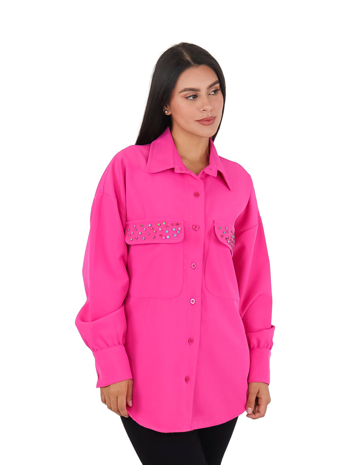 Mujer vistiendo una camisa color fucsia de manga larga con detalles de piedras en los bolsillos frontales.