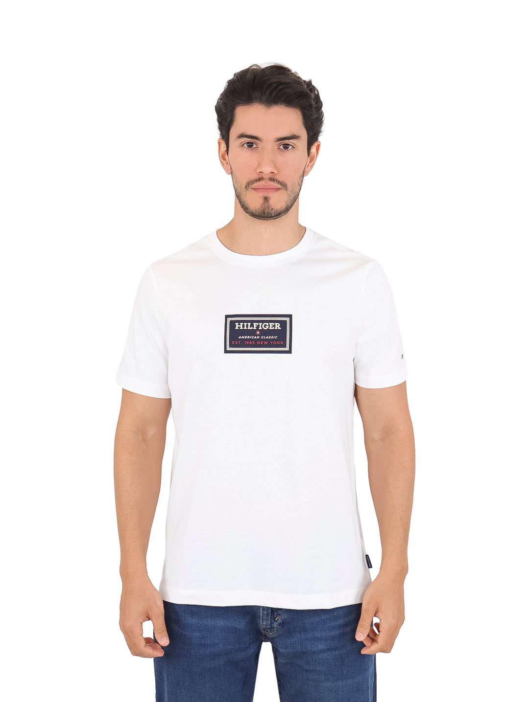 Hombre vistiendo una camiseta Tommy Hilfiger de color blanco con un estampado rectangular en el pecho.