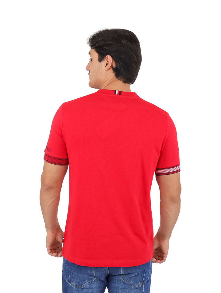 Hombre vistiendo una camiseta Tommy Hilfiger de color rojo con cuello redondo y detalles en los puños de las mangas.