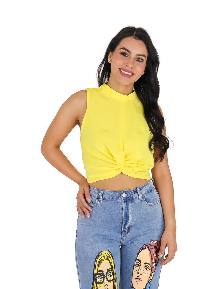 Mujer vistiendo blusa amarilla sin mangas con detalle de nudo frontal y pantalones vaqueros.