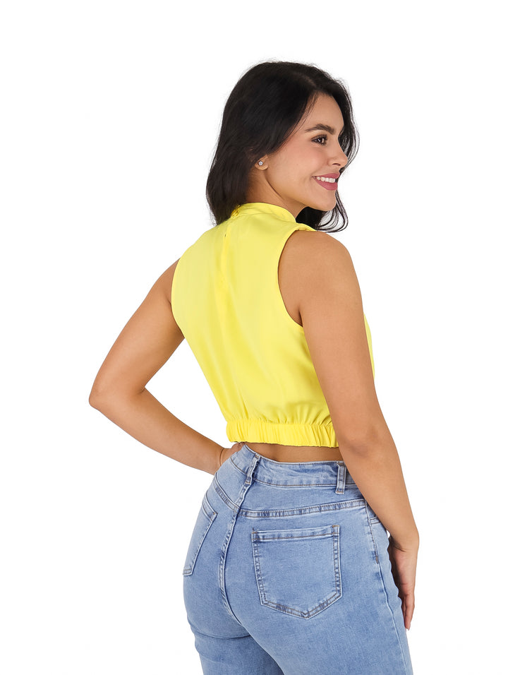Mujer vistiendo blusa amarilla sin mangas con detalle de nudo frontal y pantalones vaqueros.