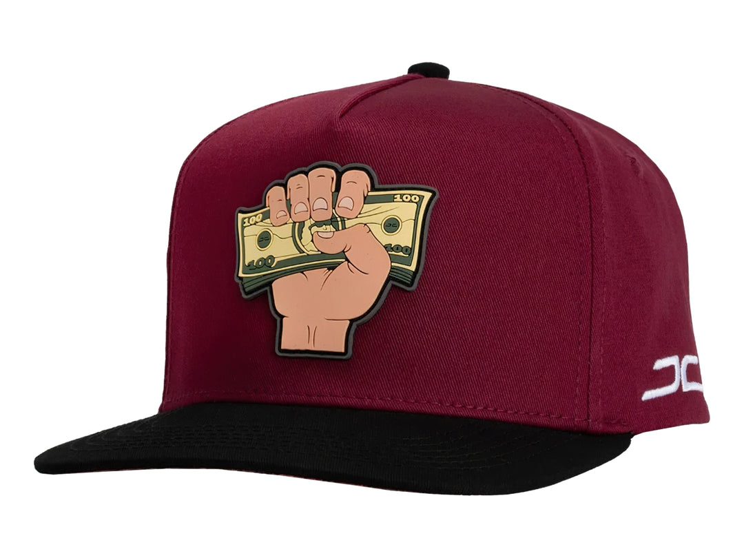 Gorra snapback color rojo con visera negra y un parche frontal de una mano sosteniendo billetes.