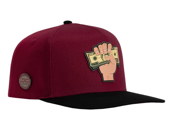 Gorra snapback color rojo con visera negra y un parche frontal de una mano sosteniendo billetes.