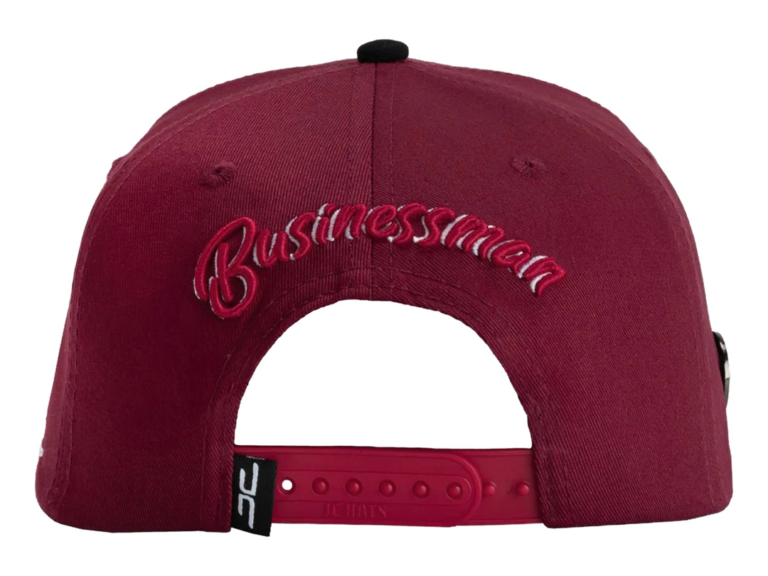 Gorra snapback color rojo con visera negra y un parche frontal de una mano sosteniendo billetes.