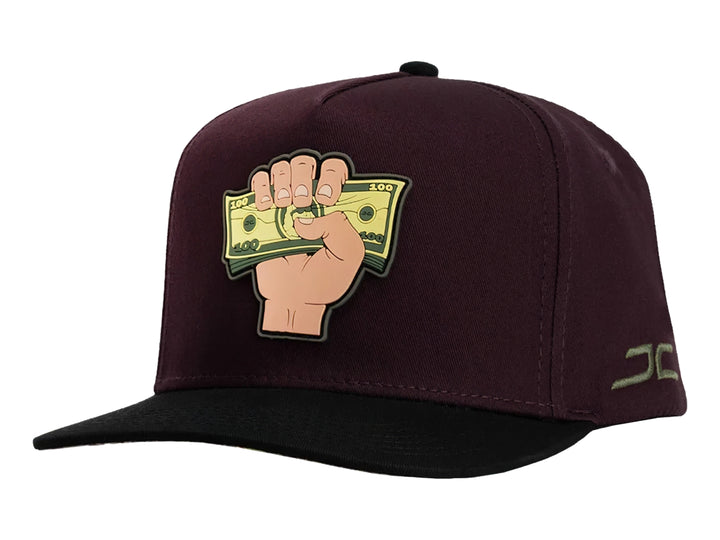Gorra snapback color burgundy con visera negra y un parche frontal de una mano sosteniendo billetes.