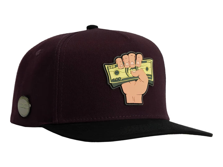 Gorra snapback color burgundy con visera negra y un parche frontal de una mano sosteniendo billetes.