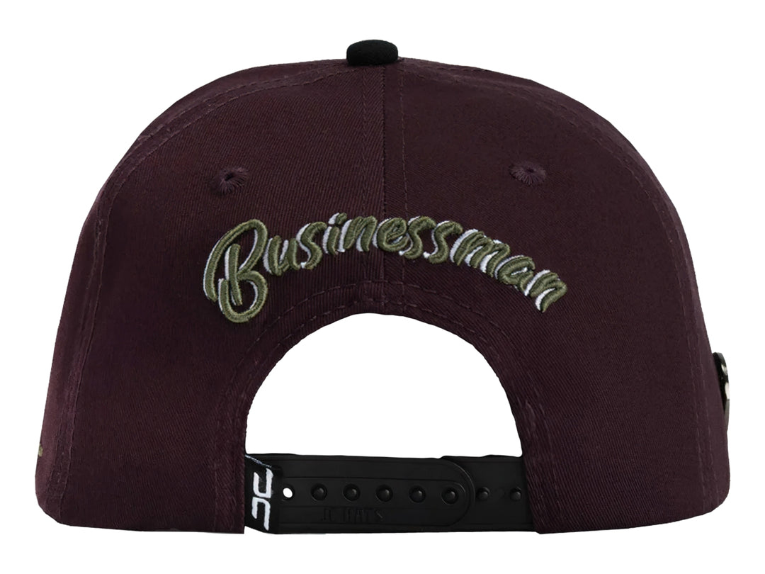 Gorra snapback color burgundy con visera negra y un parche frontal de una mano sosteniendo billetes.