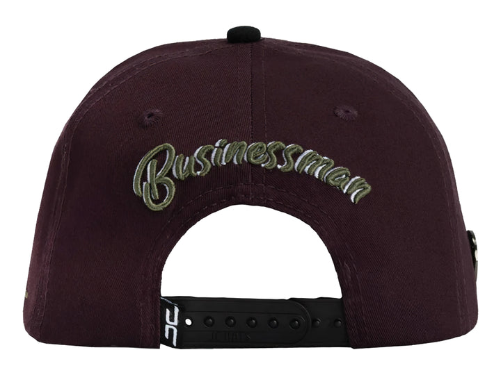 Gorra snapback color burgundy con visera negra y un parche frontal de una mano sosteniendo billetes.