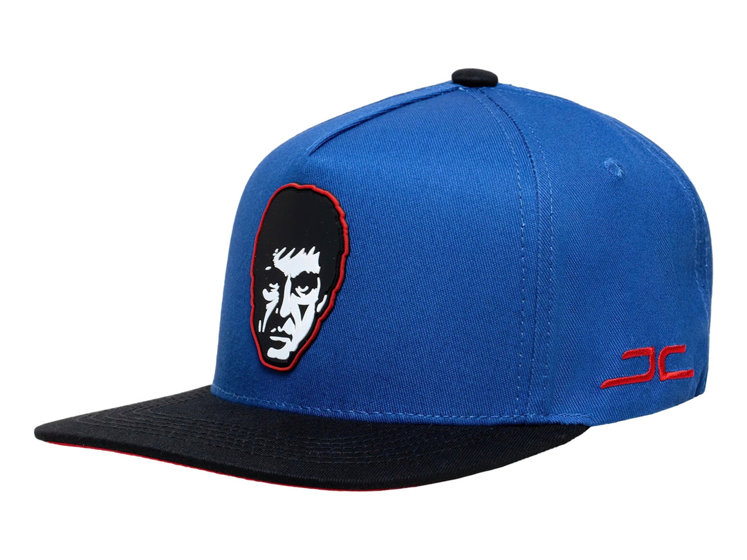 Gorra snapback azul con visera negra, presenta un bordado de rostro en el frente y logo lateral rojo.