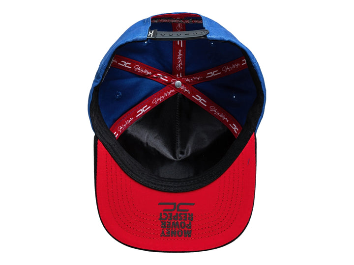 Gorra snapback azul con visera negra, presenta un bordado de rostro en el frente y logo lateral rojo.