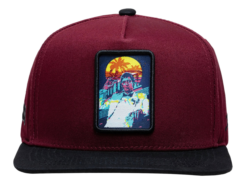 Gorra snapback color burgundy con visera negra y un parche rectangular colorido en el frente.