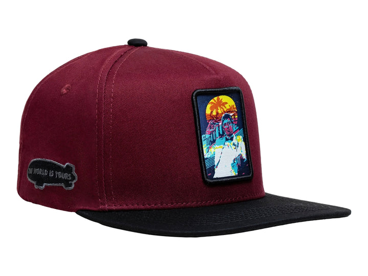 Gorra snapback color burgundy con visera negra y un parche rectangular colorido en el frente.