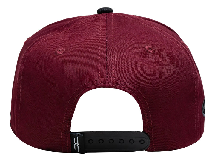 Gorra snapback color burgundy con visera negra y un parche rectangular colorido en el frente.
