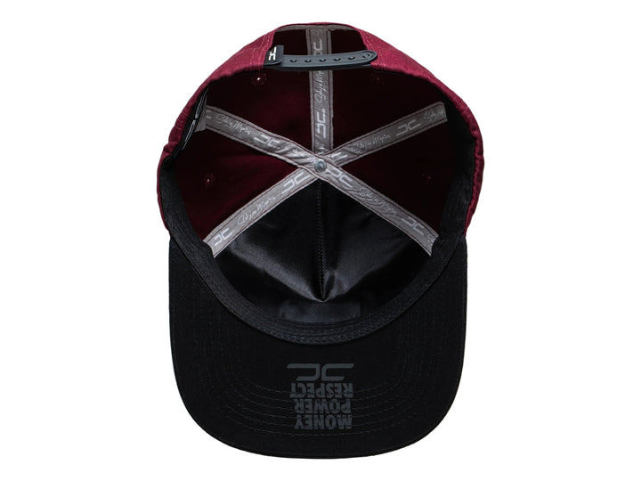 Gorra snapback color burgundy con visera negra y un parche rectangular colorido en el frente.