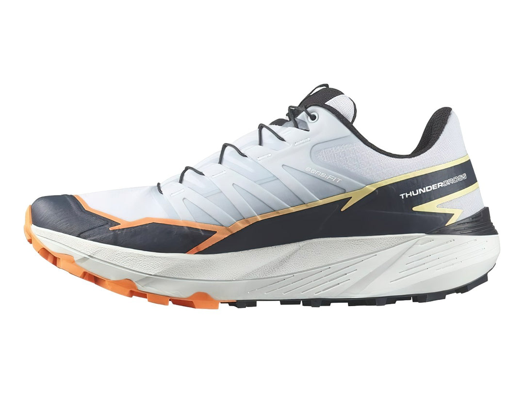 Tenis Salomon Thundercross color blanco y gris con detalles en naranja y suela para trail.