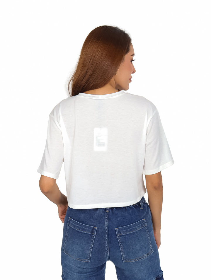 Mujer vistiendo playera corta color ivory con estampado gráfico en tonos amarillo y rosa.