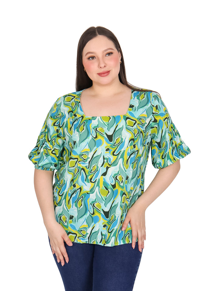 Mujer vistiendo blusa de manga corta con estampado abstracto en tonos menta, azul y amarillo.