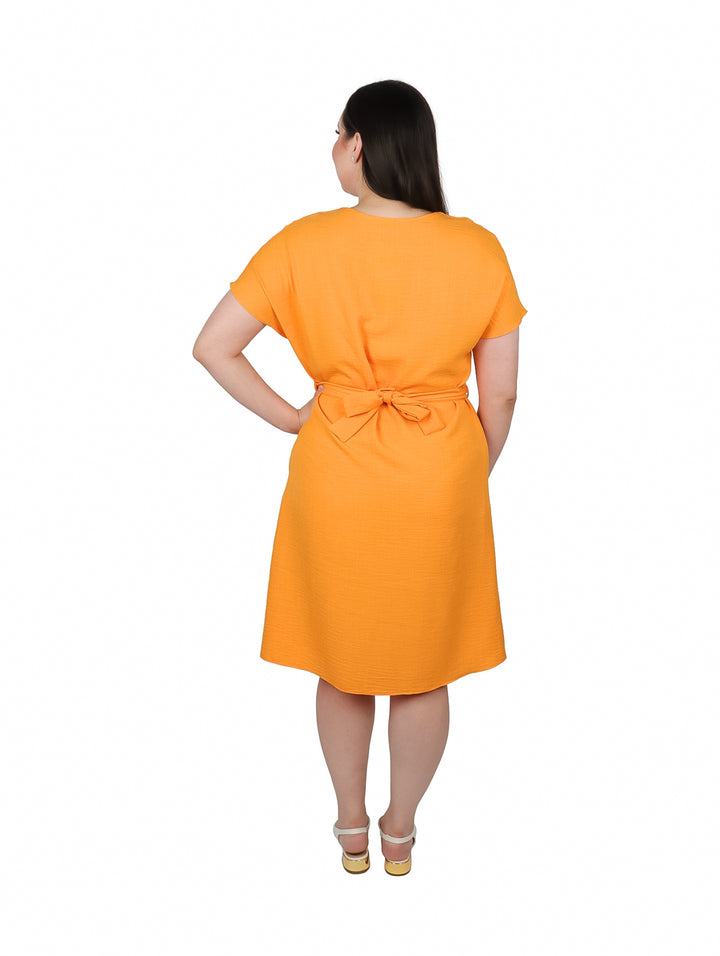 Mujer vistiendo un vestido camisero color mango con botones frontales y amarre en la cintura.