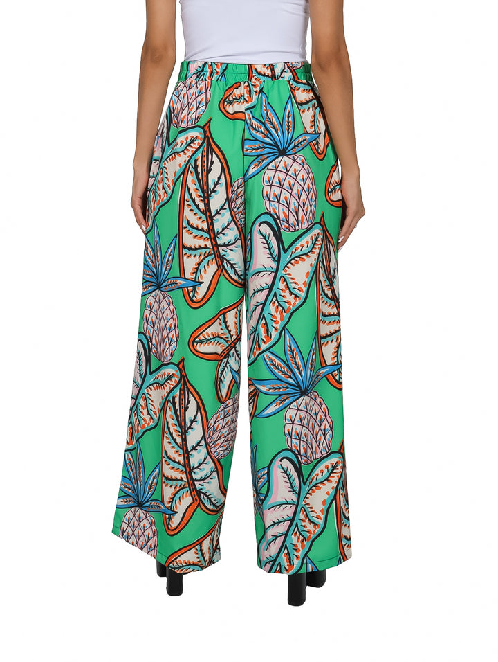 Pantalón ancho color verde con estampado tropical de piñas y hojas en tonos naranja y azul.