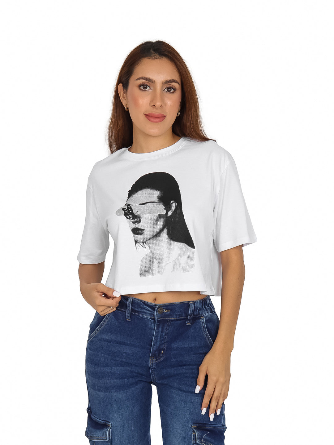 Mujer vistiendo playera corta blanca con estampado de rostro en blanco y negro y pantalones cargo azules.